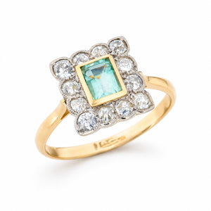 Angled product view of an antique emerald cluster ring, with a rectangular mint green gemstone surrounded by old-mine cut diamonds.