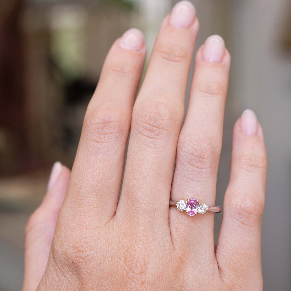 An image of a Vintage 1990s pink sapphire and diamond three-stone engagement ring in platinum worn on the hand and shown at a distance to show the proportions.  