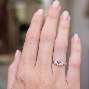 An image of a Vintage 1990s pink sapphire and diamond three-stone engagement ring in platinum worn on the hand and shown at a distance to show the proportions.  