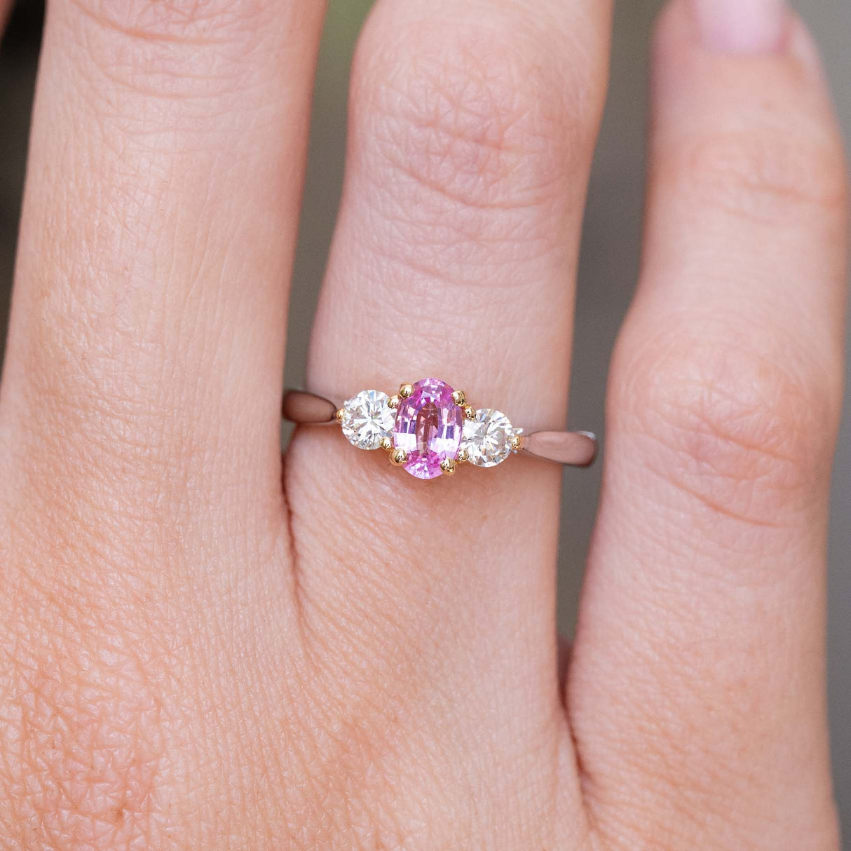 Vintage, 1990s pink sapphire and diamond three-stone engagement ring being worn on the finger and shown up close.
