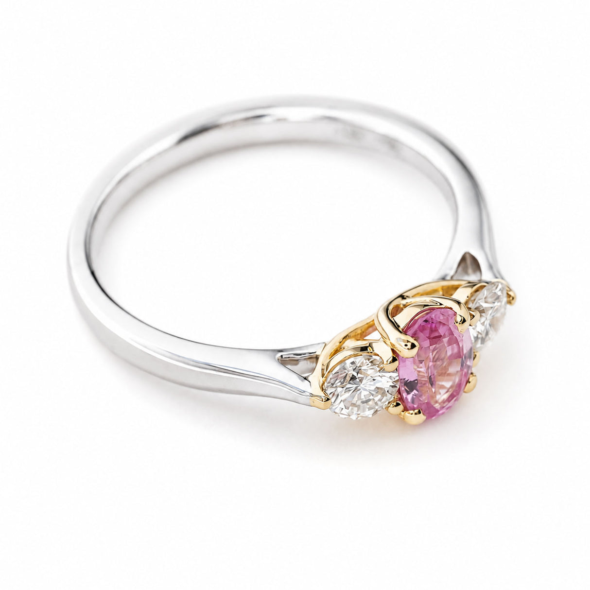 A Vintage, 1990s platinum three-stone engagement ring with a central pink sapphire, flanked by two diamonds, shown from above to see the yellow gold setting the gemstones are in.