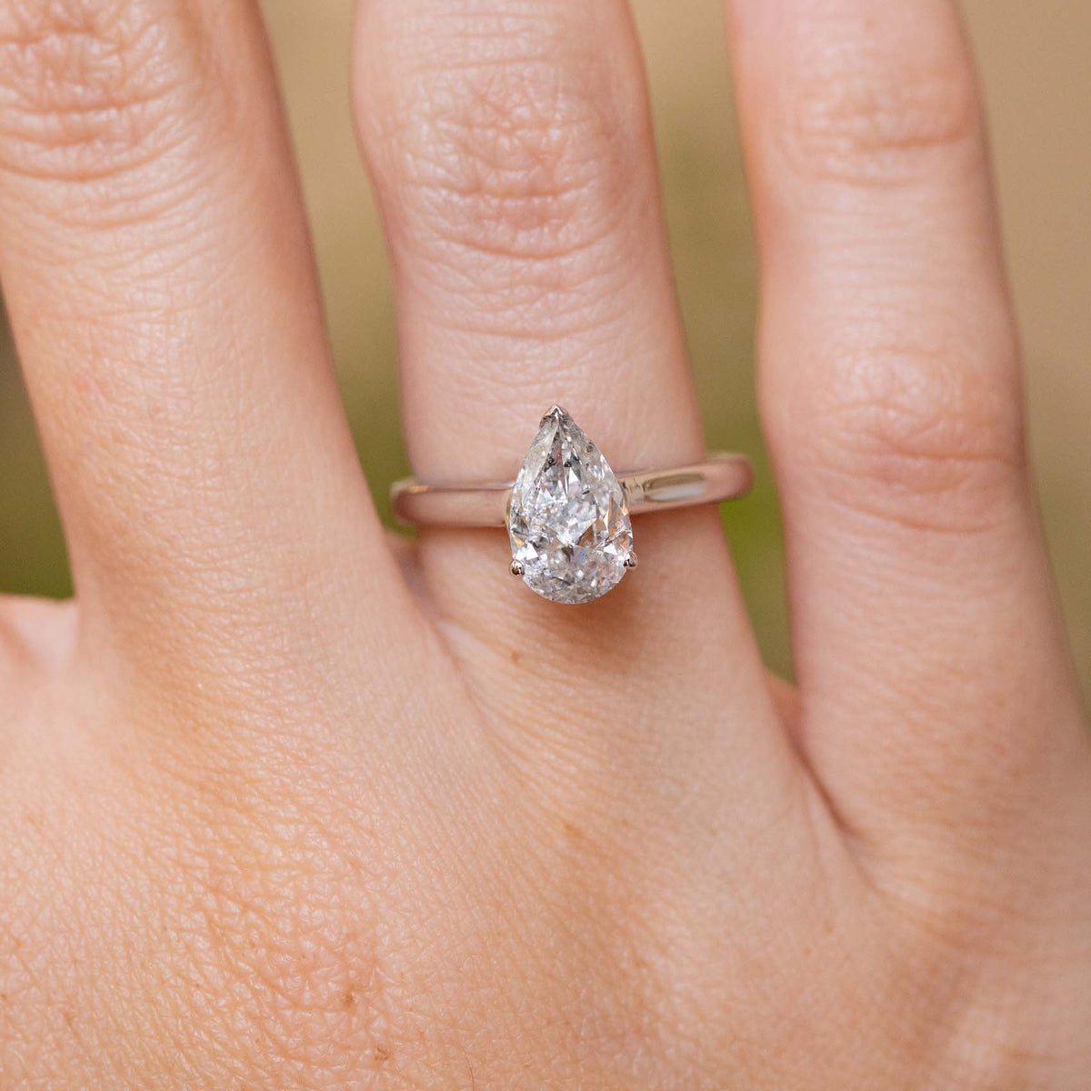 Close-up of a 1990s white gold solitaire ring featuring a pear-shaped salt and pepper diamond in a delicate claw setting.