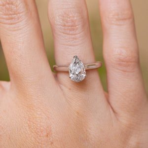 Close-up of a 1990s white gold solitaire ring featuring a pear-shaped salt and pepper diamond in a delicate claw setting.