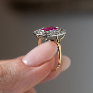 Side profile of an antique Edwardian Burmese ruby and diamond cluster ring held between fingers, displaying the elevated platinum setting, open gallery and split-shoulder yellow gold band.