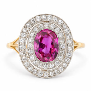 Antique Edwardian Burmese ruby and diamond cluster engagement ring in yellow gold and platinum, featuring an oval old-cut pinkish-red ruby surrounded by two concentric halos of sparkling diamonds.