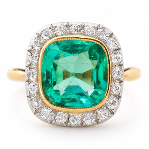 An Antique, Belle Époque cushion-cut Colombian emerald and diamond coronet cluster engagement ring in yellow gold shown against a plain white background.