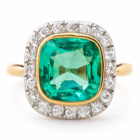 An Antique, Belle Époque cushion-cut Colombian emerald and diamond coronet cluster engagement ring in yellow gold shown against a plain white background.