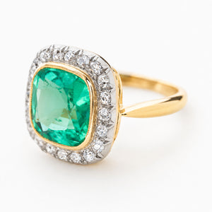 An Antique Victorian cushion-cut Colombian emerald and diamond coronet cluster engagement ring in yellow gold shown at an angle against a plain white background to show the setting style.