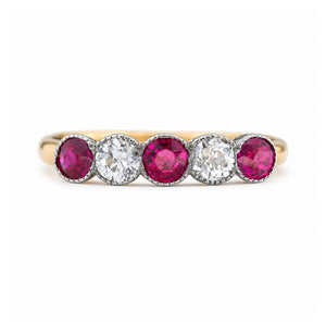 A close-up of an Antique, Edwardian pink-ruby and old-cut diamond five-stone ring with a platinum setting and a yellow gold band.