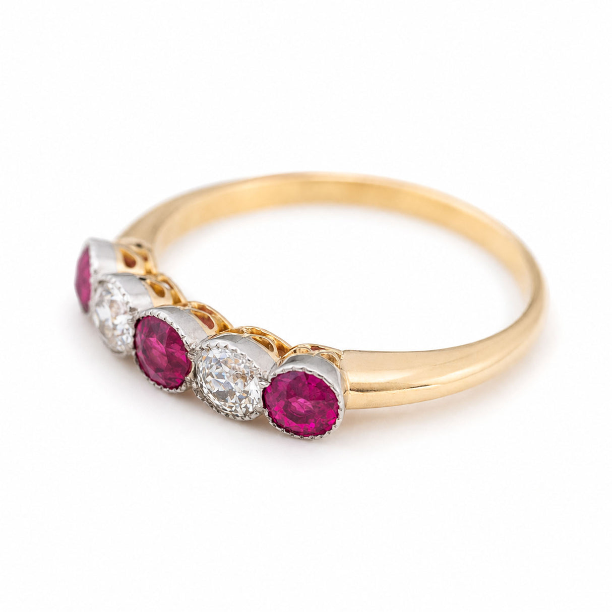 A three-quarter close-up of an Antique, Edwardian pink-ruby and old-cut diamond five-stone ring with a platinum setting and a yellow gold band with a pierced gallery.