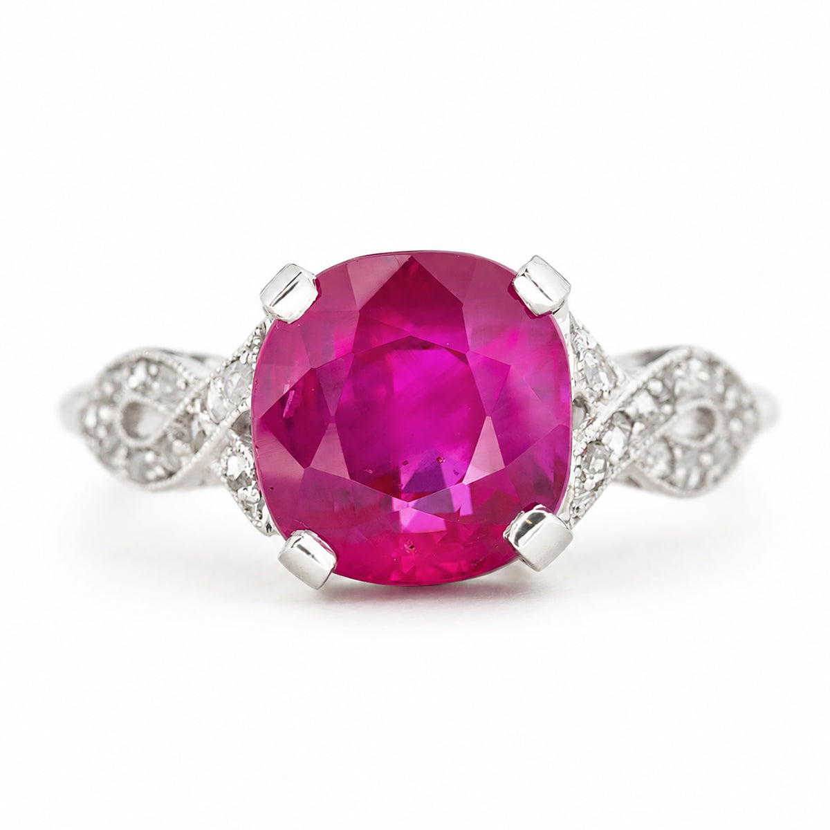 A cushion-cut Burmese pink ruby Art Deco engagement ring with pavé diamonds set either side into the white gold band. Shown on a plain white background. 