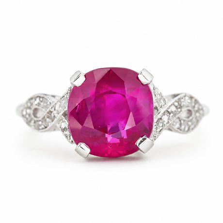 A cushion-cut Burmese pink ruby Art Deco engagement ring with pavé diamonds set either side into the white gold band. Shown on a plain white background. 