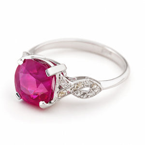 An Antique, 1920s Art Deco engagement ring,  featuring a large, cushion-cut pink Ruby in a prong setting, with an ornate diamond-accented white gold band, shown on a white background.