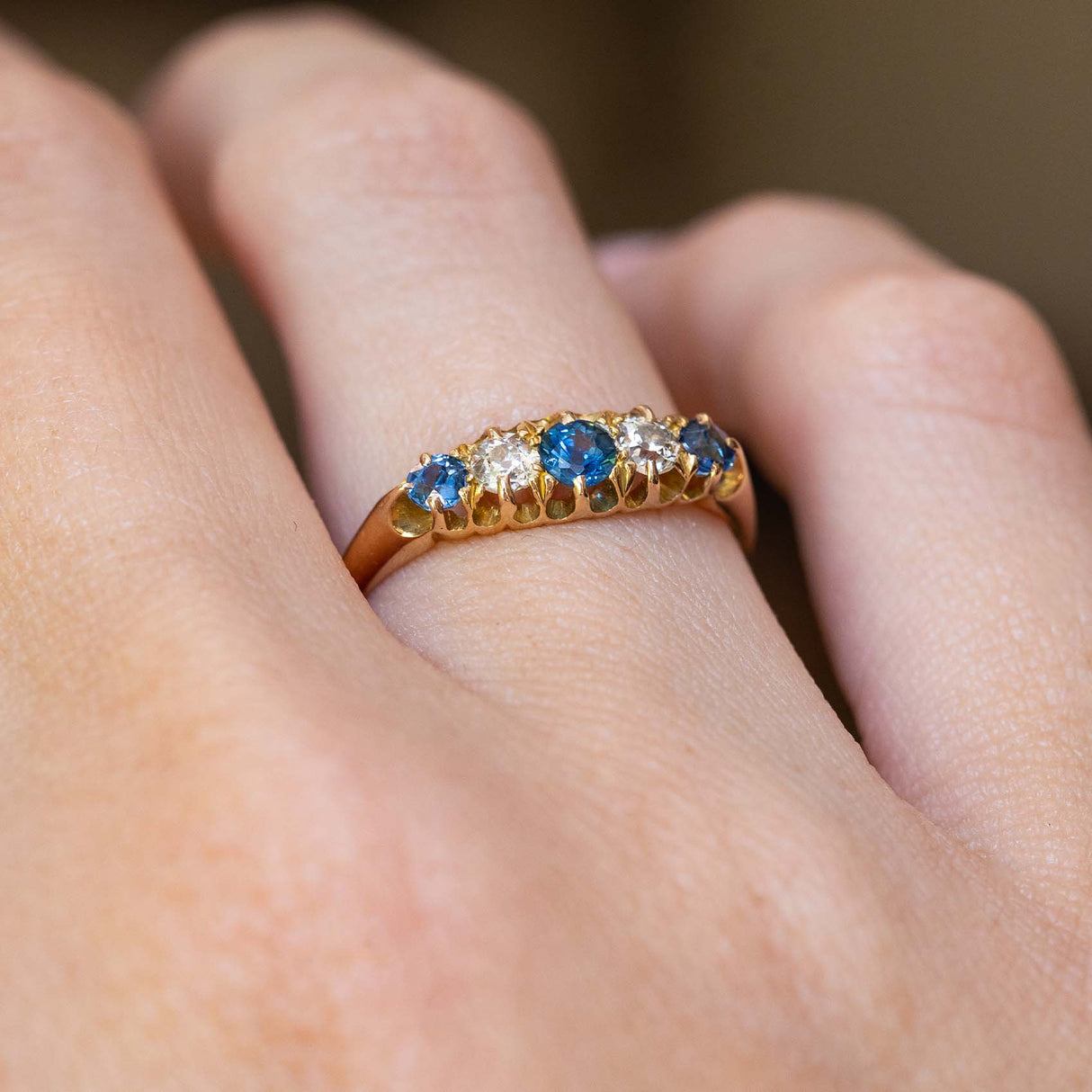 An antique Edwardian sapphire and diamond five-stone ring worn on the finger.