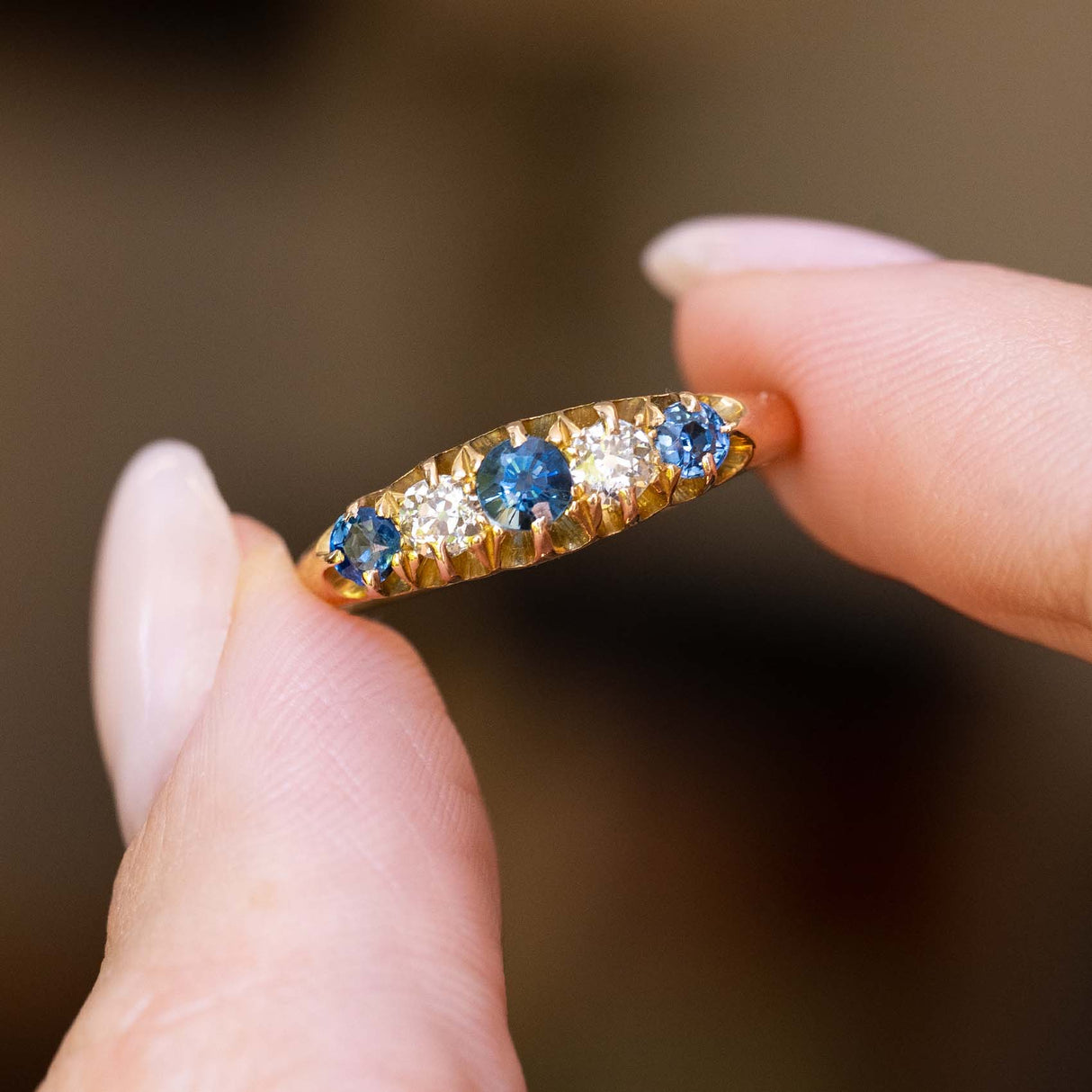 An antique Edwardian sapphire and diamond five-stone ring held between the fingers.
