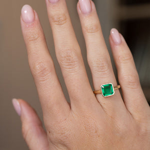 Antique-inspired emerald engagement ring worn on the hand, showing the elegant proportions of its square solitaire design.