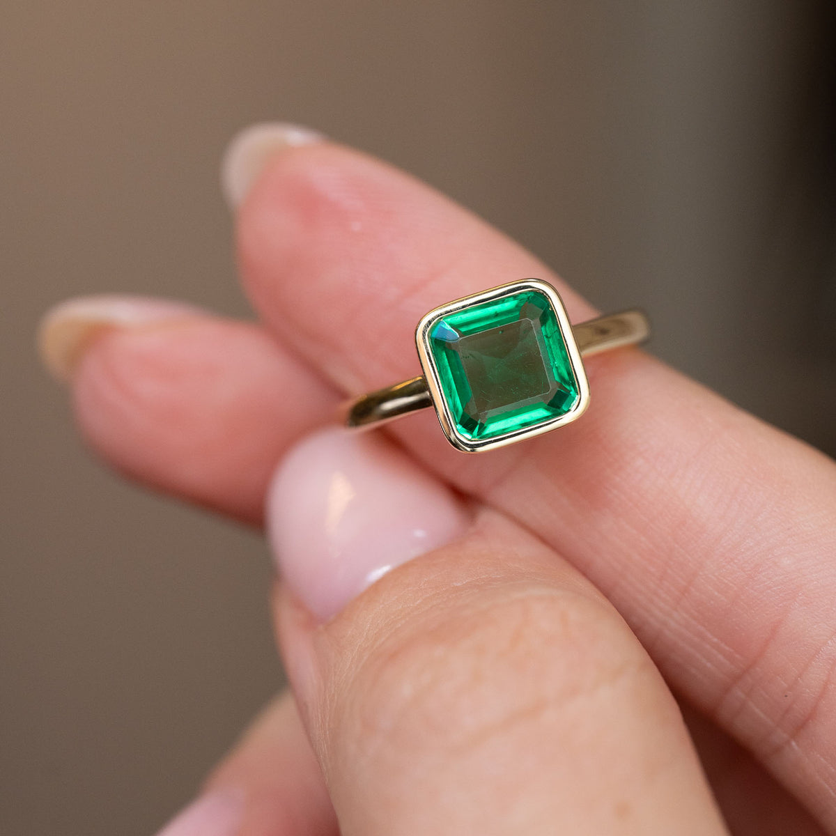 Handheld close-up of the square-shaped emerald-cut solitaire and warm yellow gold surround.