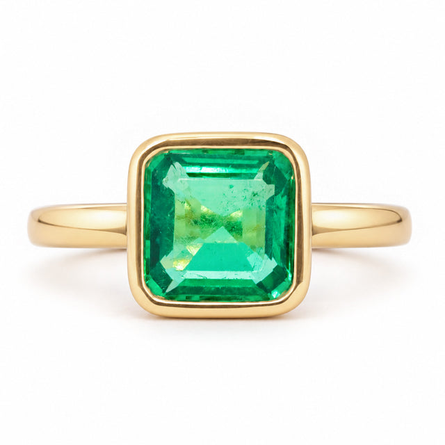 Antique-inspired Colombian emerald solitaire engagement ring in yellow gold, featuring a square emerald-cut stone in a smooth rub-over setting.