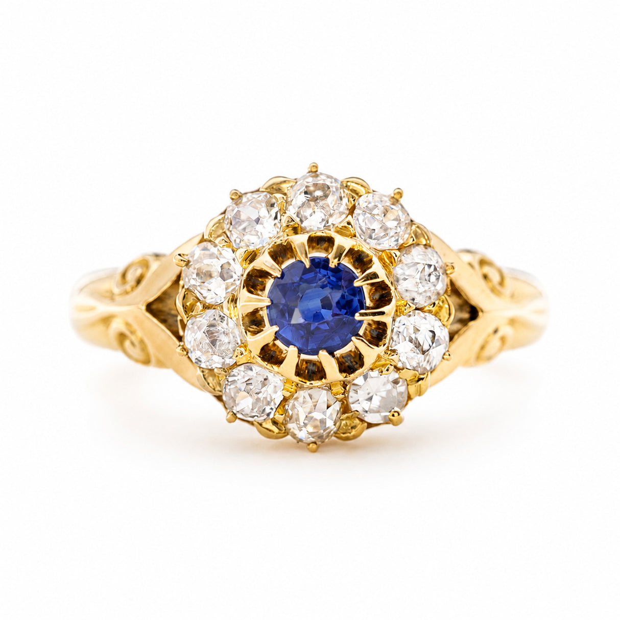 An Antique, Victorian sapphire and old cut diamond cluster ring in yellow gold featuring decorative shoulders shown against a plain white background.