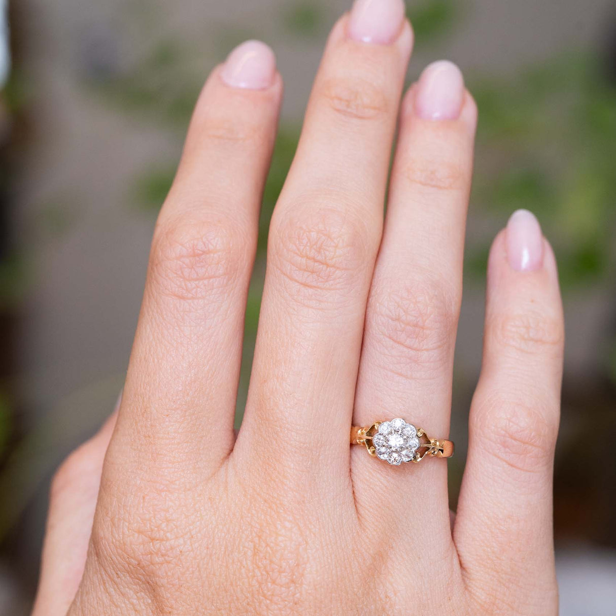 An image of an outstretched hand wearing an antique yellow gold engagement ring designed as a diamond cluster, worn on the finger to show the proportions.