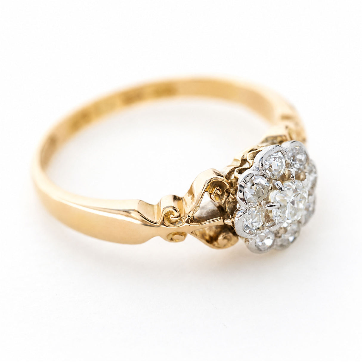 An antique engagement ring made in the Edwardian era designed as a daisy cluster ring shown from the side against a plain white background.