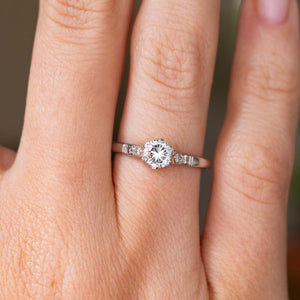 A close-up of a hand wearing a platinum Antique, 1930s Art-Deco diamond solitaire engagement ring showcasing both the central diamond and flanking diamonds.