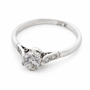 A three-quarter view of an  Art-Deco platinum ring set with a natural round diamond at the centre.  