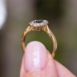 A close-up photograph of an Antique Edwardian sapphire and diamond cluster engagement ring in yellow gold held up and shown from the side to display the pierced open-work gallery of the ring against a blurred background.