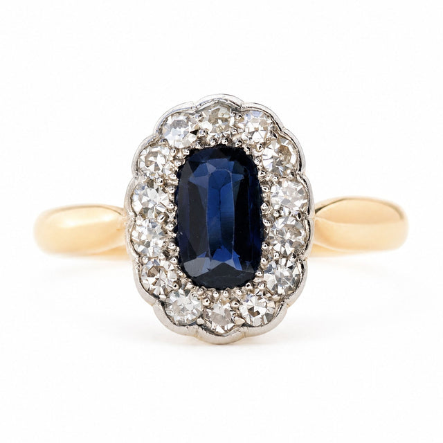 An Antique Edwardian Sapphire and Diamond Cluster engagement Ring set on a yellow gold band, photographed on a white background.