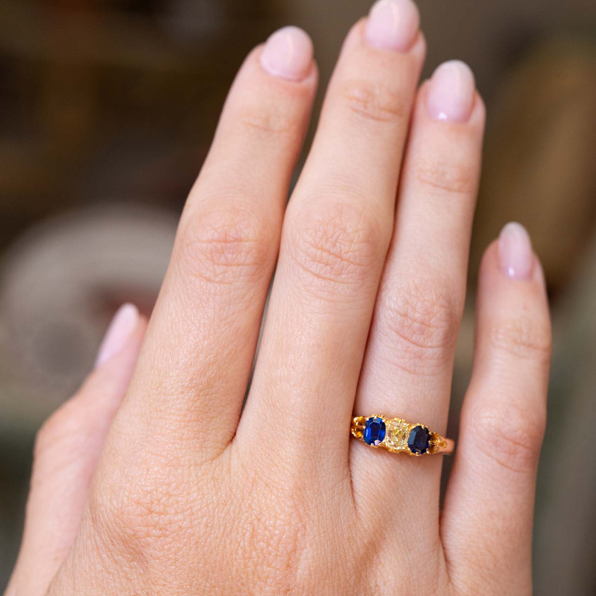 An image of an Antique, Victorian blue sapphire and yellow diamond three-stone engagement ring mounted in yellow gold and worn on an outstretched hand to show off the proportions of the ring.
