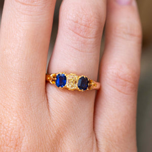 A close-up picture of a hand wearing an Antique, Victorian blue sapphire and yellow elongated cushion-cut  diamond three-stone engagement ring.