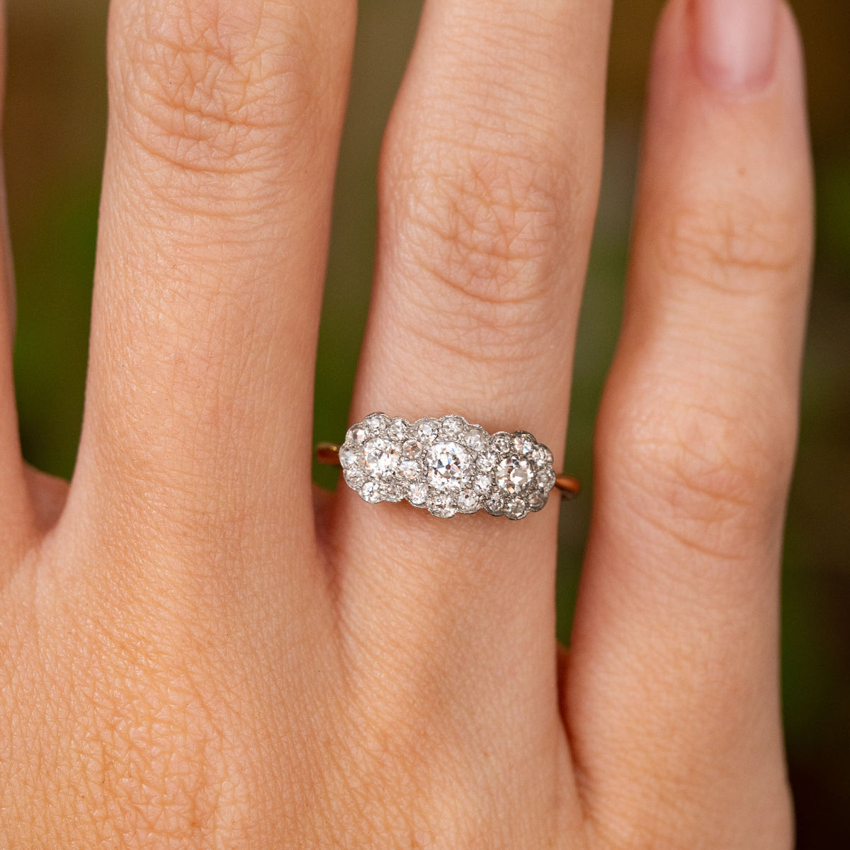 Close-up of an antique diamond triple-cluster ring with grain-set old-cut diamonds and fine millegrain detailing.