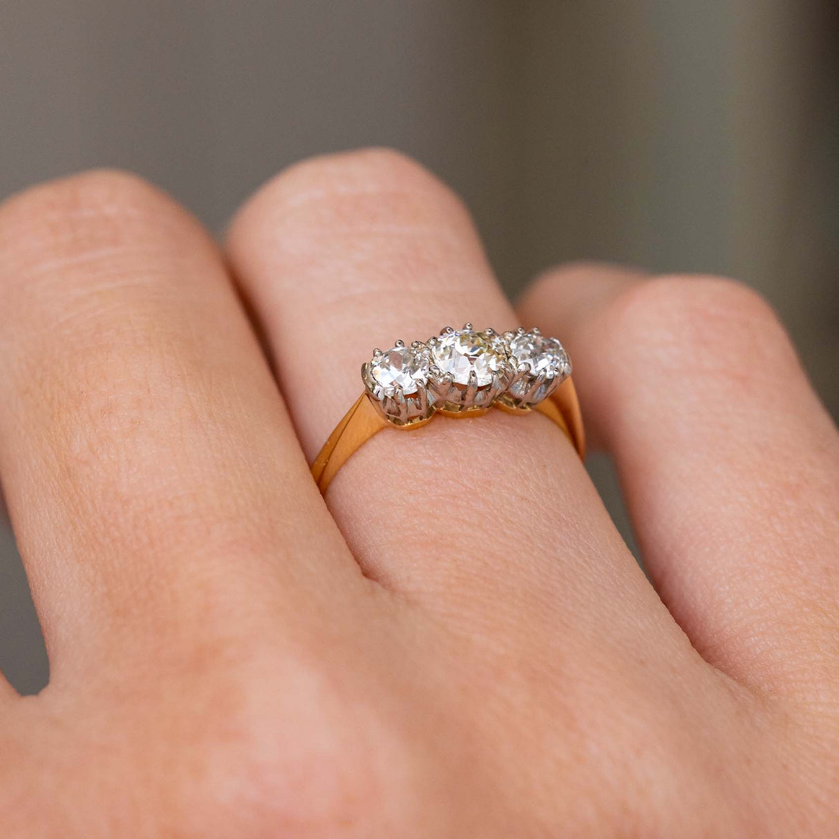 A close up picture of an Antique, Edwardian diamond trilogy yellow gold engagement ring worn on hand and showed from an angle to show the gallery