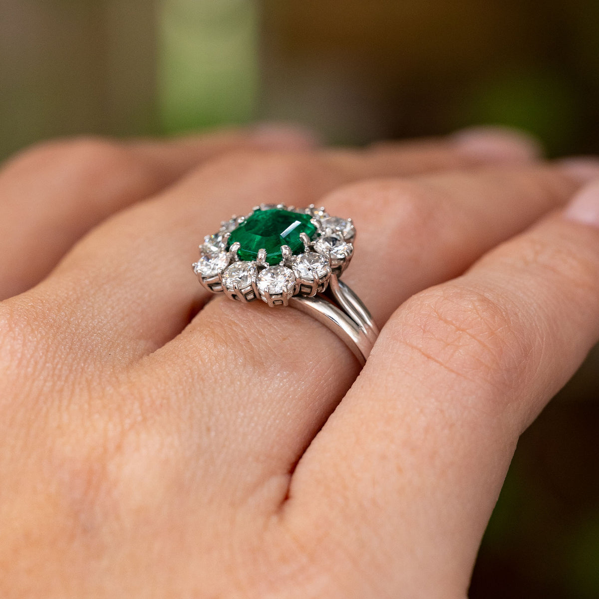 A close up image of a Vintage, 1950s emerald and diamond cluster cocktail engagement ring in white gold shown from a low angle to show off the gallery
