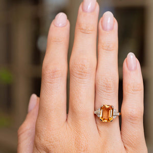 A Vintage, 1950s orange topaz and diamond ring in yellow gold worn on the hand from a distance.