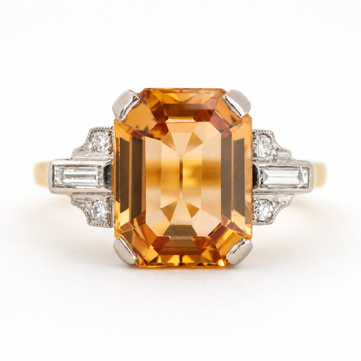 A vintage emerald-cut orange topaz ring with diamond-set shoulders shown photographed on a clean white background.