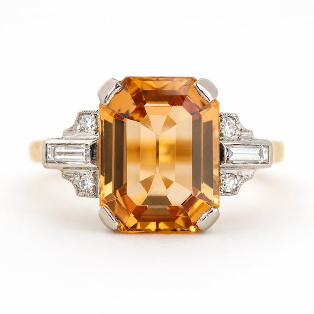 A vintage emerald-cut orange topaz ring with diamond-set shoulders shown photographed on a clean white background.