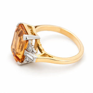 A yellow gold vintage engagement ring with orange topaz and diamonds shown from an elevated angle against a white background.