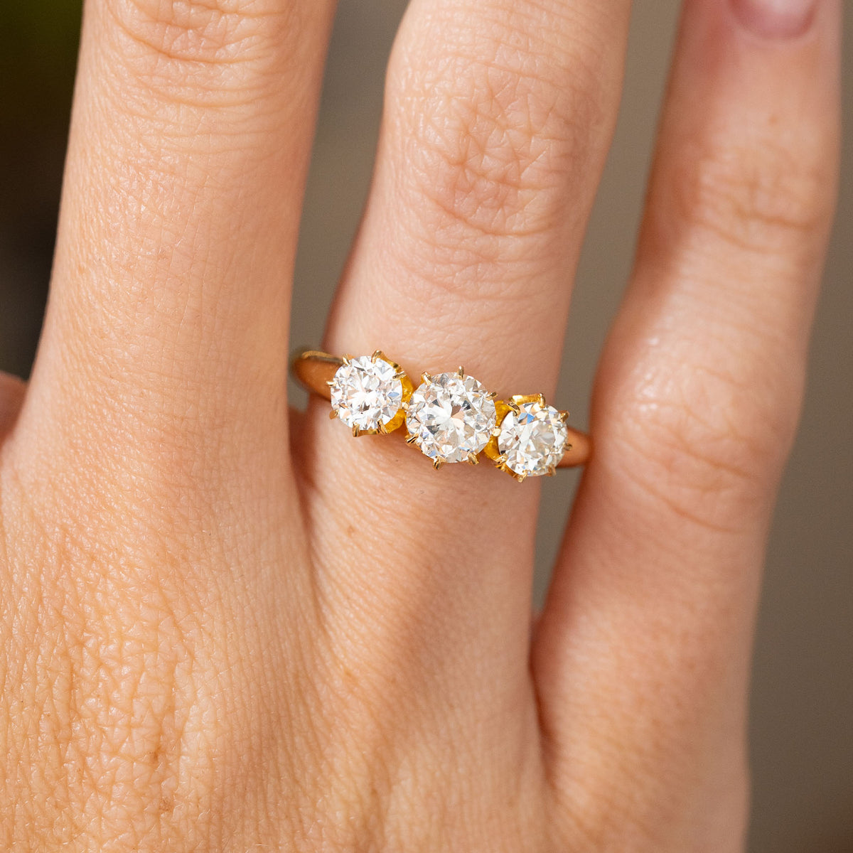 Close-up of a vintage 18ct yellow gold engagement ring on the finger, set with a transitional-cut centre diamond between two old-cut diamonds.