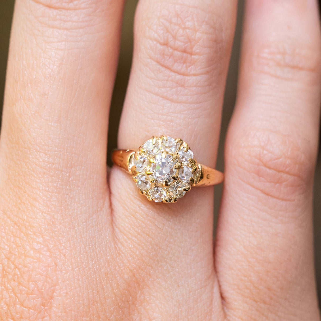 A close-up of a hand wearing an antique Victorian era yellow gold old-cut diamond coronet cluster engagement ring.