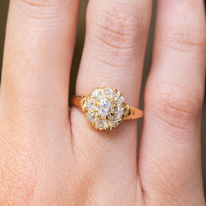 A close-up of a hand wearing an antique Victorian era yellow gold old-cut diamond coronet cluster engagement ring.