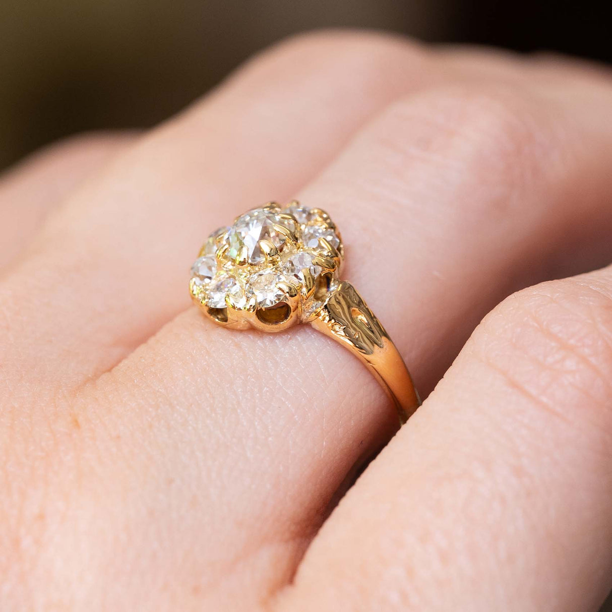 A detailed image taken at a low angle of an antique Victorian era yellow gold old-cut diamond coronet cluster engagement ring worn on the hand and shown on the hand from an angle to show the gallery.