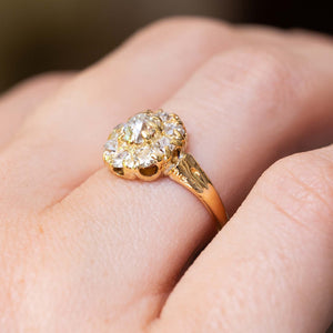 A detailed image taken at a low angle of an antique Victorian era yellow gold old-cut diamond coronet cluster engagement ring worn on the hand and shown on the hand from an angle to show the gallery.