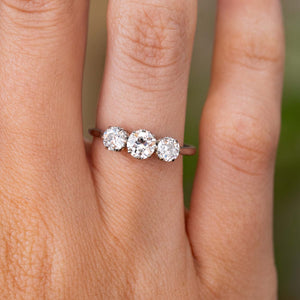 A close-up of a hand wearing an Antique, Edwardian diamond trilogy engagement ring made in platinum.