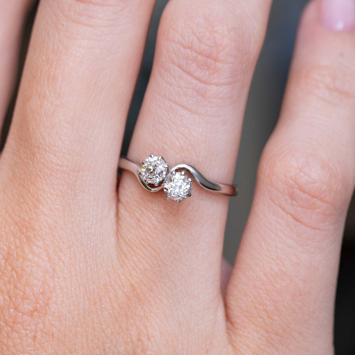 A close-up image of a hand wearing a platinum Antique, Edwardian toi et moi diamond engagement ring with a curved platinum band. 