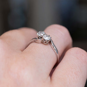 A close-up image of an Antique, Edwardian toi et moi diamond engagement ring in platinum worn on a person's finger seen from a low angle to show the setting style of the diamonds.
