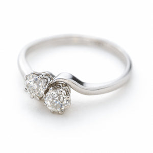 A platinum Antique, Edwardian toi et moi two stone diamond engagement ring photographed on a clean white background and seen from a slightly elevated angle. 