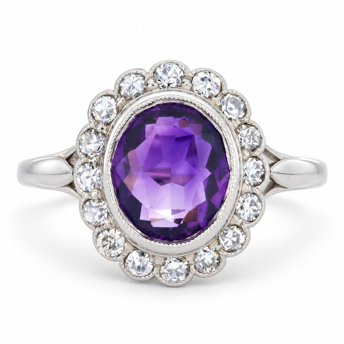 Rich oval amethyst surrounded by a scalloped cluster of old-cut diamonds in an antique Edwardian white gold and platinum ring.