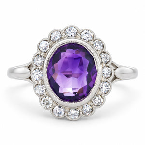 Rich oval amethyst surrounded by a scalloped cluster of old-cut diamonds in an antique Edwardian white gold and platinum ring.