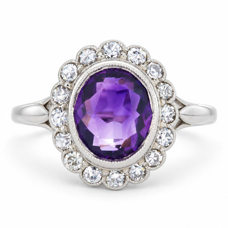 Rich oval amethyst surrounded by a scalloped cluster of old-cut diamonds in an antique Edwardian white gold and platinum ring.